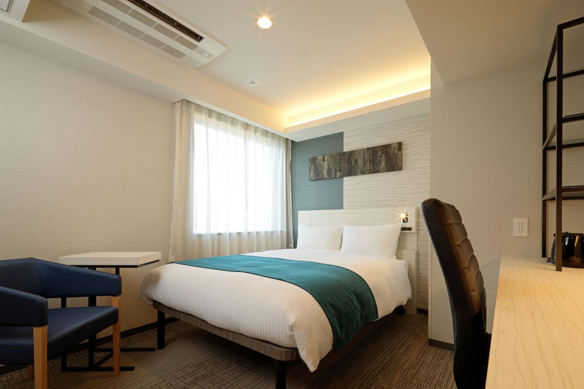 A hotel room with a bed, a desk, a chair, and a window with curtains.