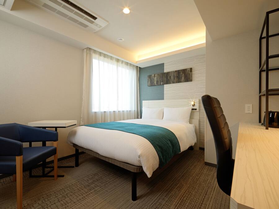 A hotel room with a bed, a desk, a chair, and a window with curtains.