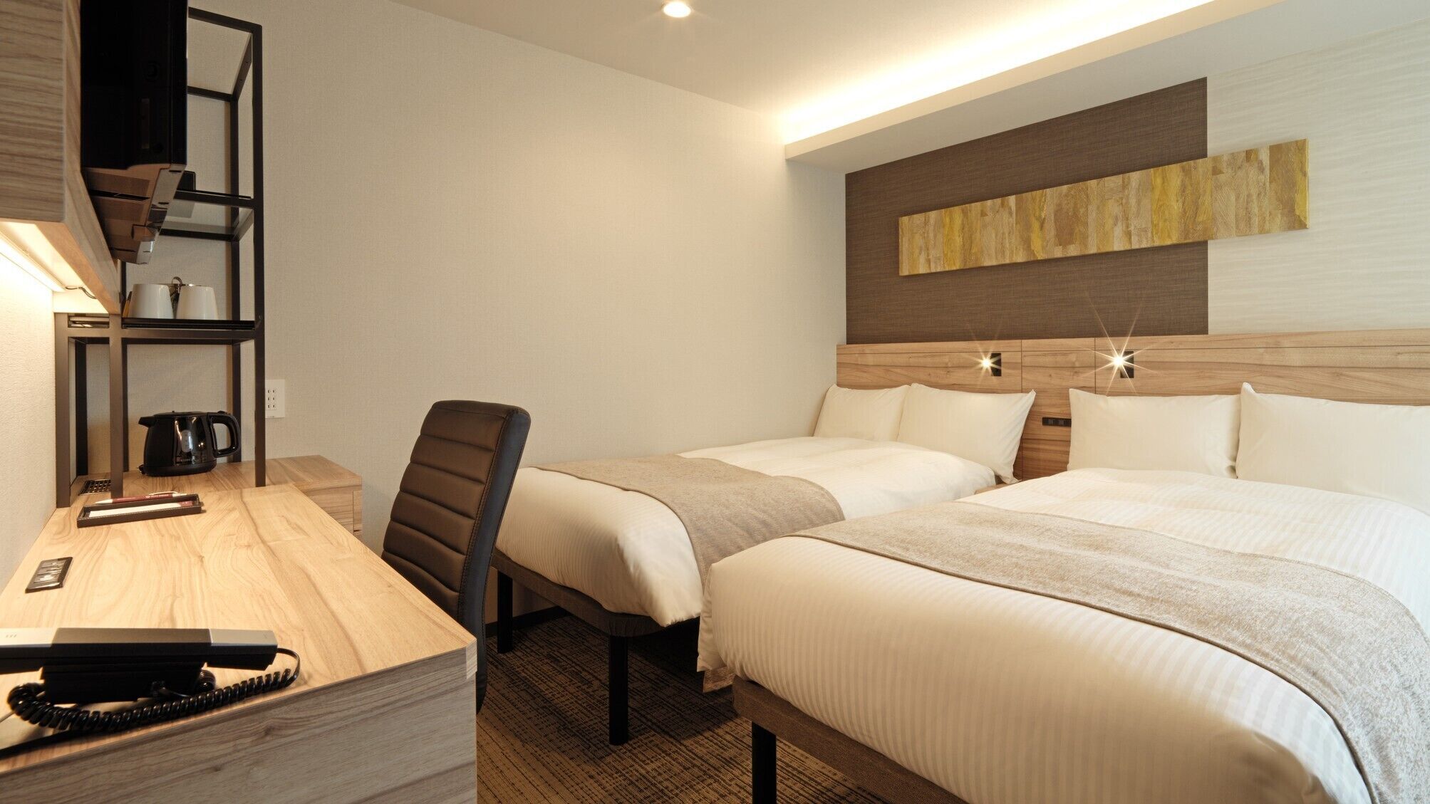 A hotel room with a desk, chair, two beds, a coffee maker, and a wall art piece.