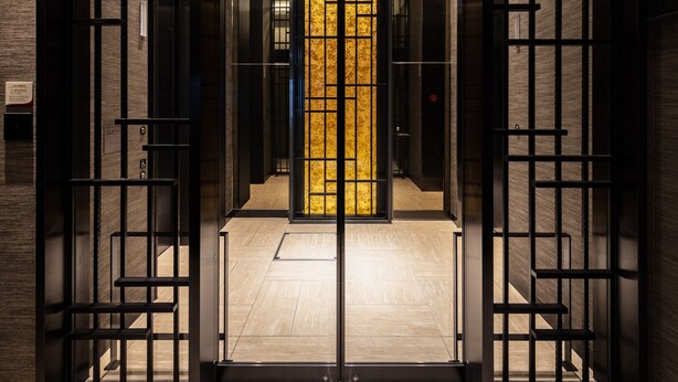 Vista interna de um elevador moderno com porta de vidro e interior dourado.