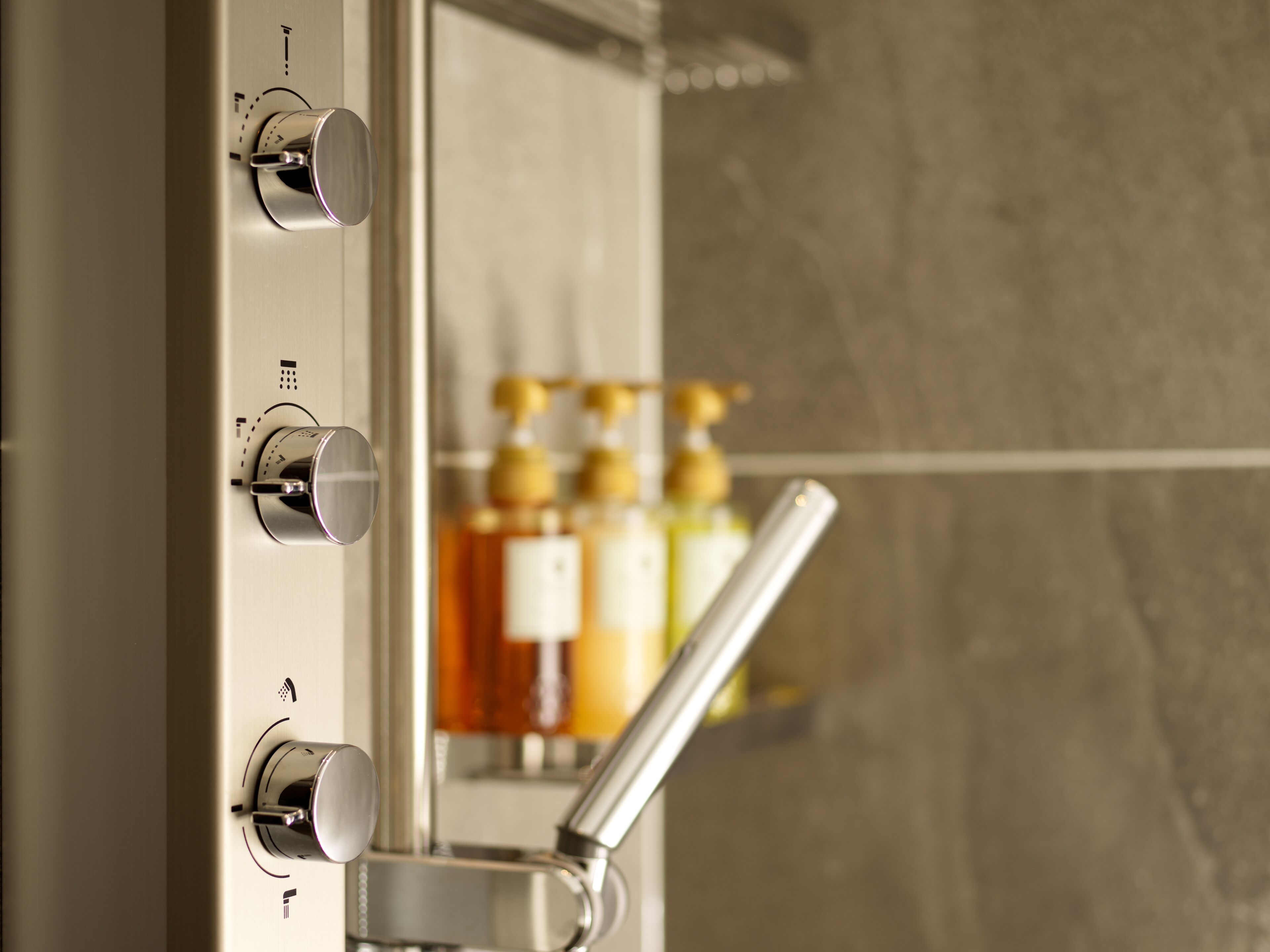 A bathroom with a modern shower control panel and a visible bottle of shampoo.
