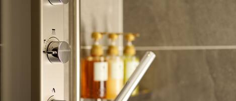A bathroom with a modern shower control panel and a visible bottle of shampoo.