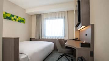 A hotel room with a bed, a desk with a chair, a television, and a window with curtains.