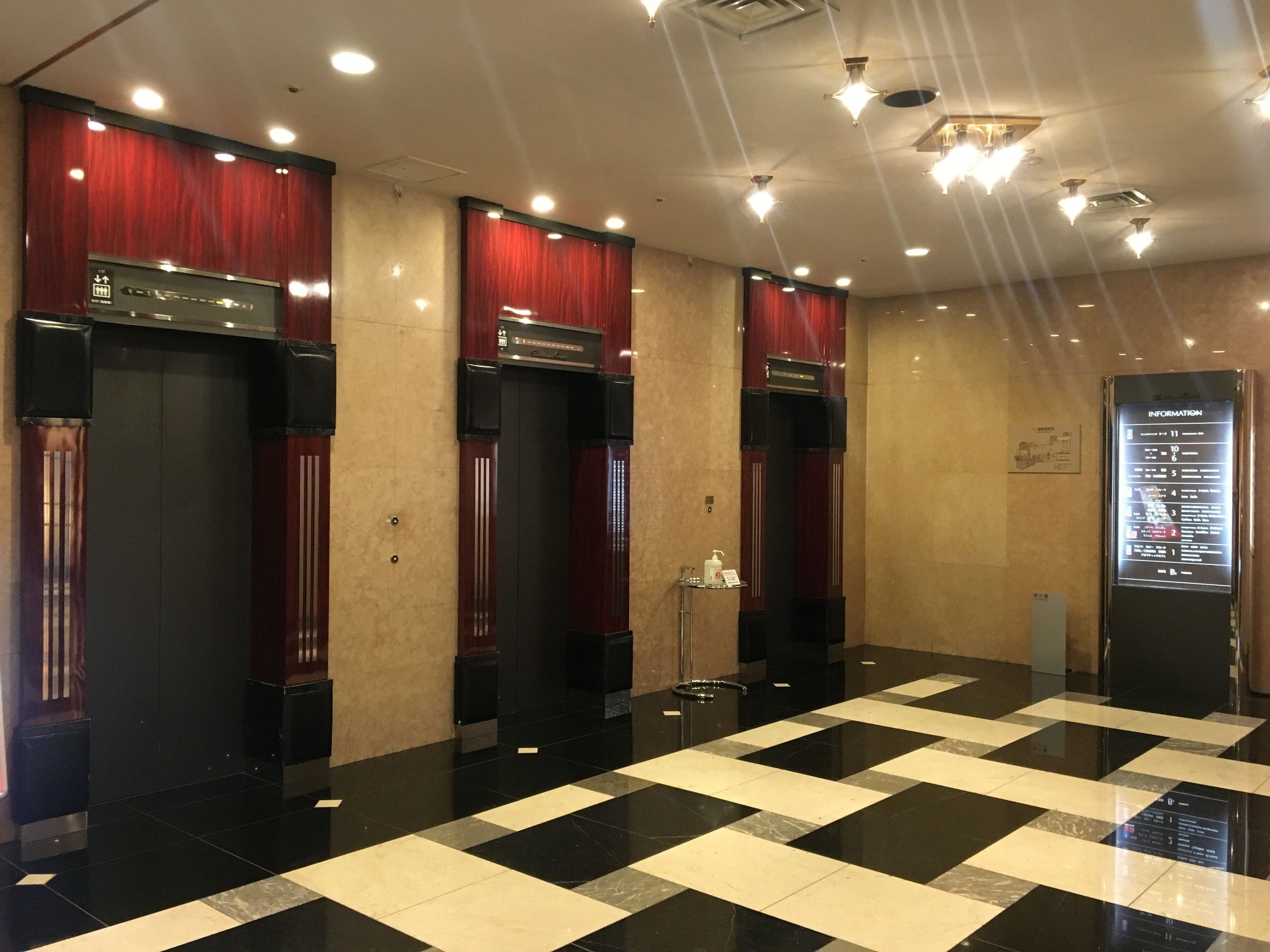 Un hall con suelo a cuadros, ascensores y un panel informativo digital.