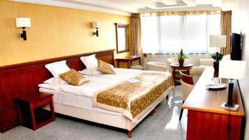 A hotel room with a large bed, a desk, a chair, a small table, and a TV.