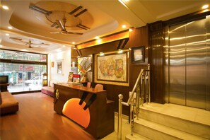 A reception area with a wooden reception desk, a staircase, and a view of the street outside. - Hotel Grand Park Inn (New Delhi)