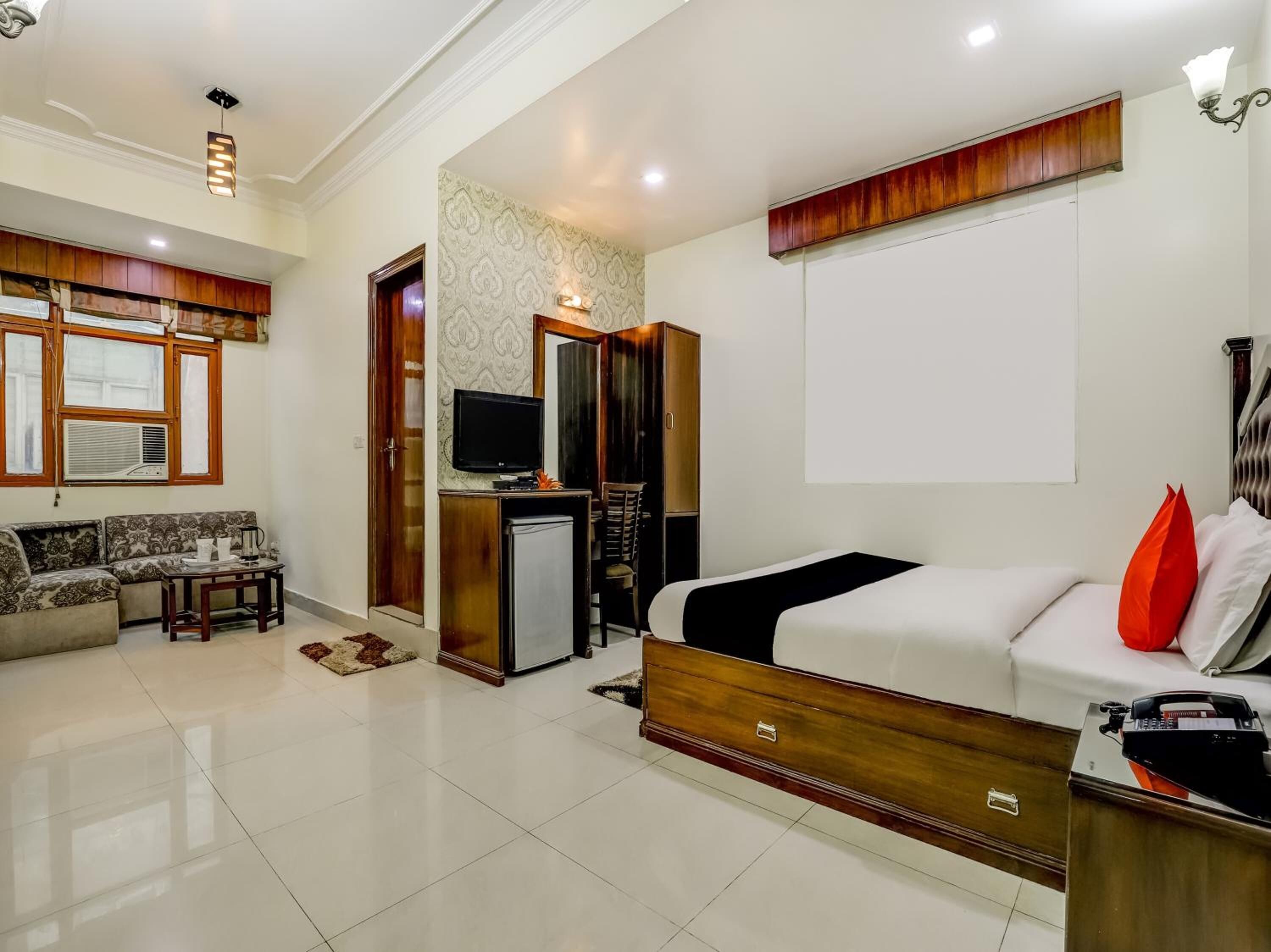 A modern hotel room with a sofa, a bed, a desk with a computer, and a television.