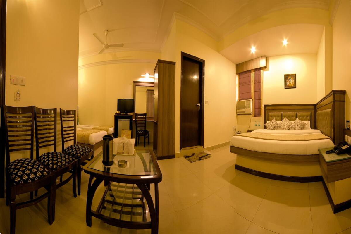 A hotel room with a bed, a desk, chairs, a television, a ceiling fan, and a door.