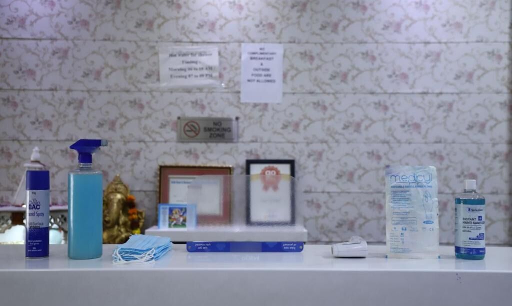 A bathroom counter with a no smoking sign, a framed certificate, a blue bottle, a face mask, a toothbrush, and a hand sanitizer bottle.