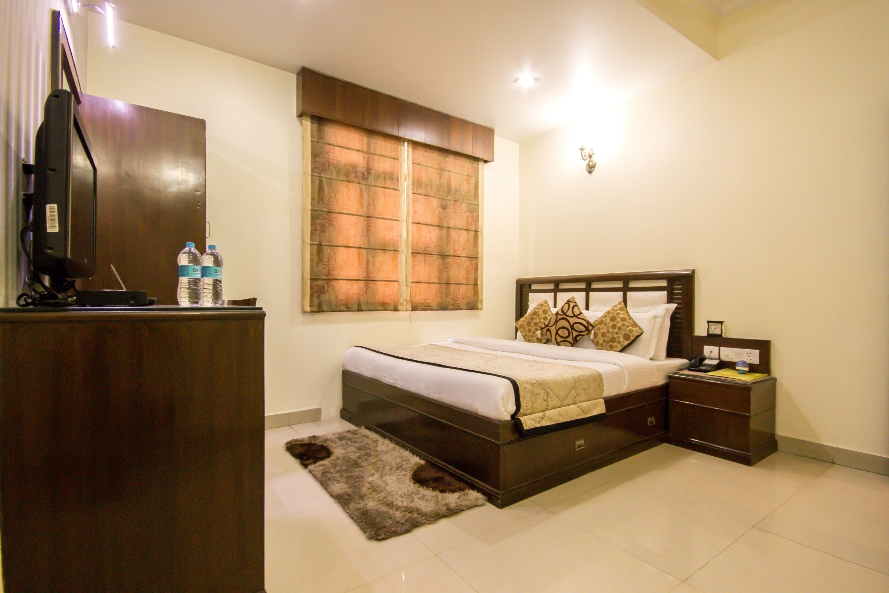 A bedroom with a bed, bedside table, nightstand, and a television on a stand.