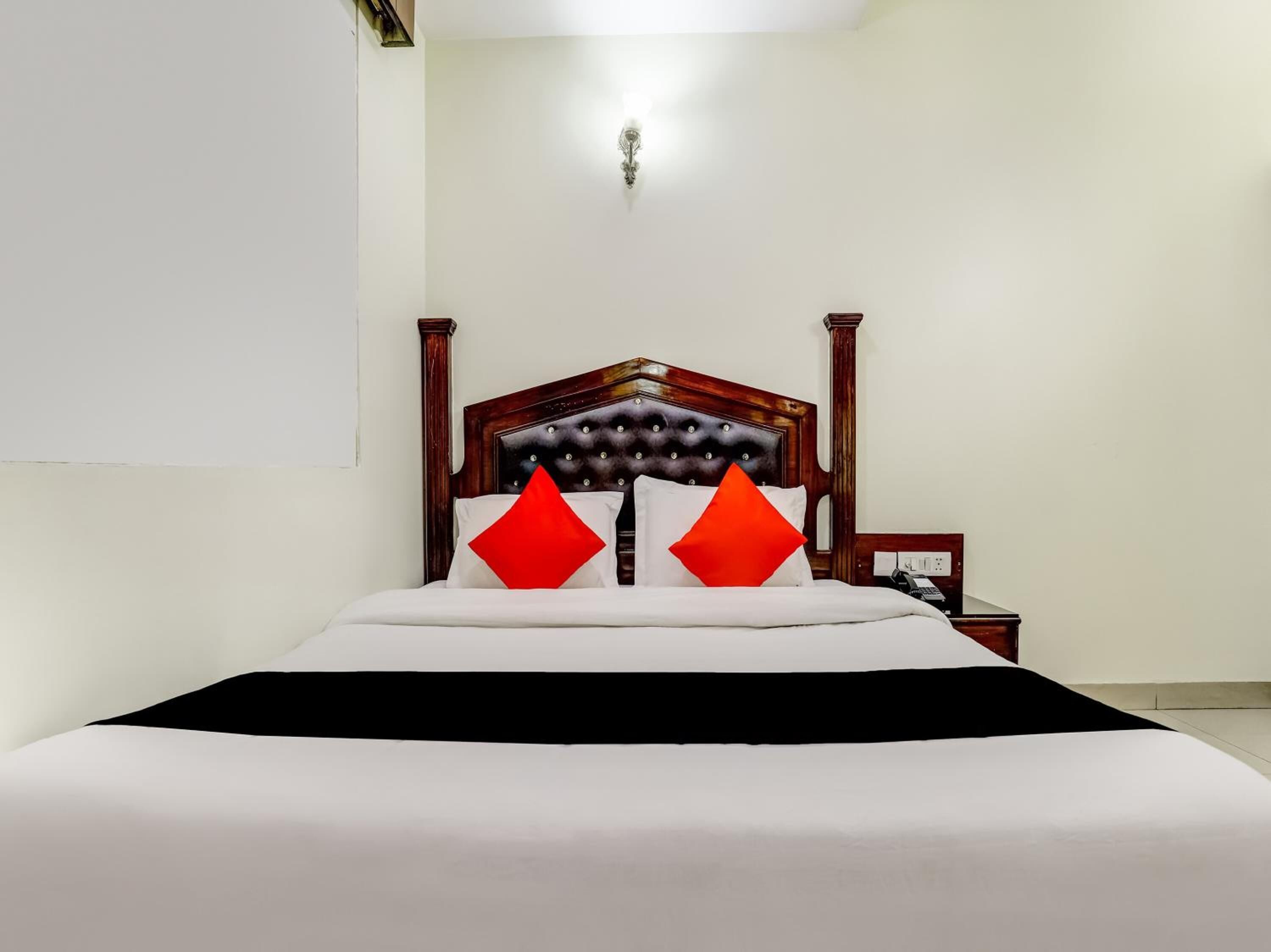 Una cama bien tendida con cabecera de madera, ropa de cama blanca y dos almohadas rojas.