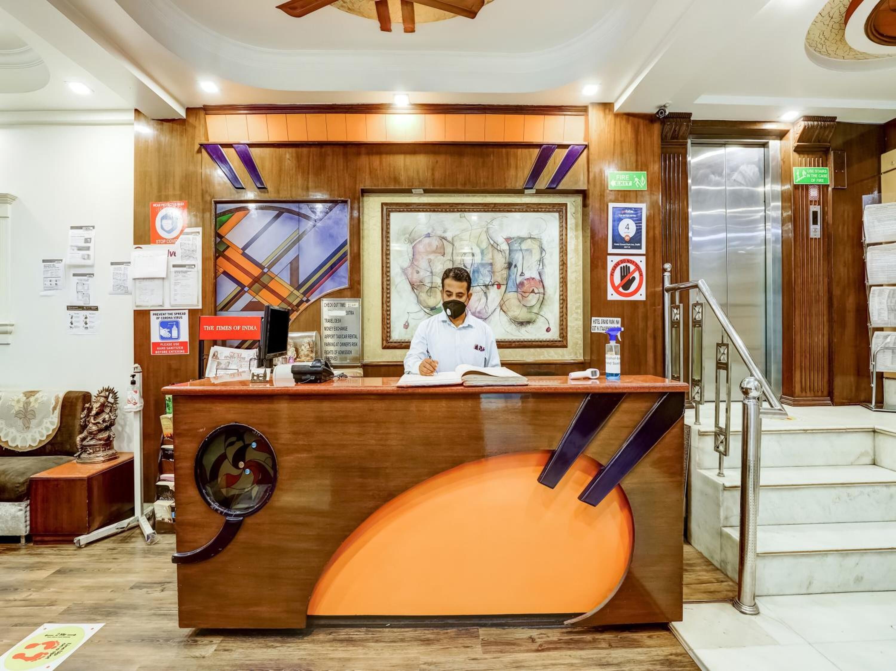 A reception desk with a wooden finish, a large abstract painting, and a digital screen displaying 'THE TIMES OF INDIA'.