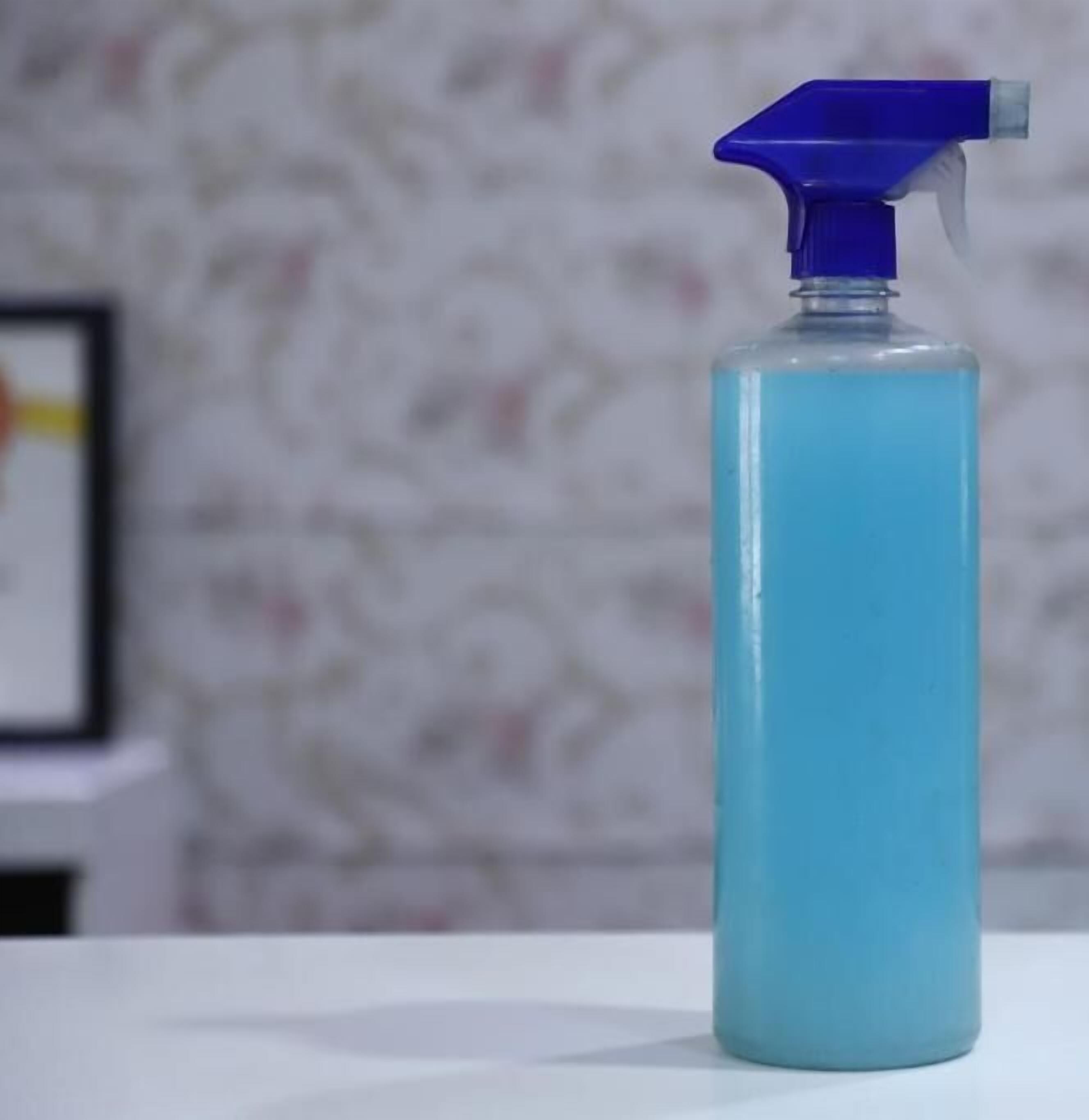 A spray bottle with a blue liquid on a white surface.