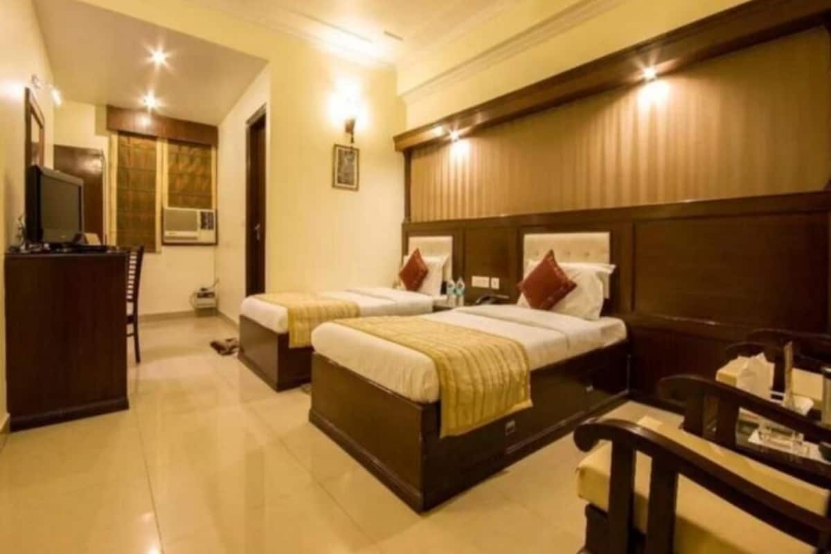 A hotel room with two beds, a desk, a chair, and a television.