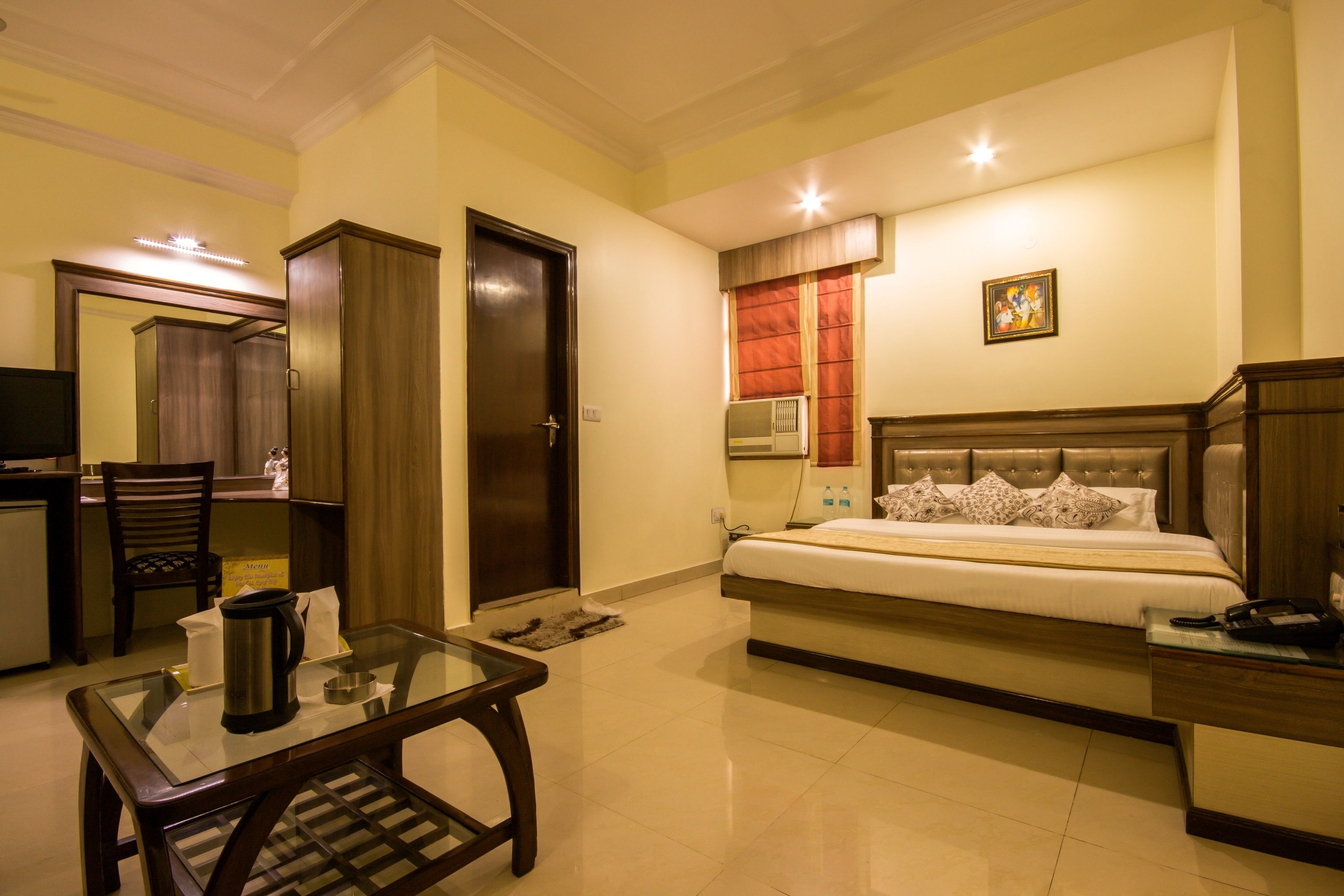 A hotel room with a bed, a desk, a chair, a coffee maker, and a TV.
