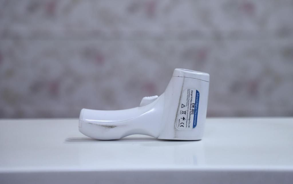A white, plastic, single-use medical device, likely a metered-dose inhaler, on a white surface with a blurred background.