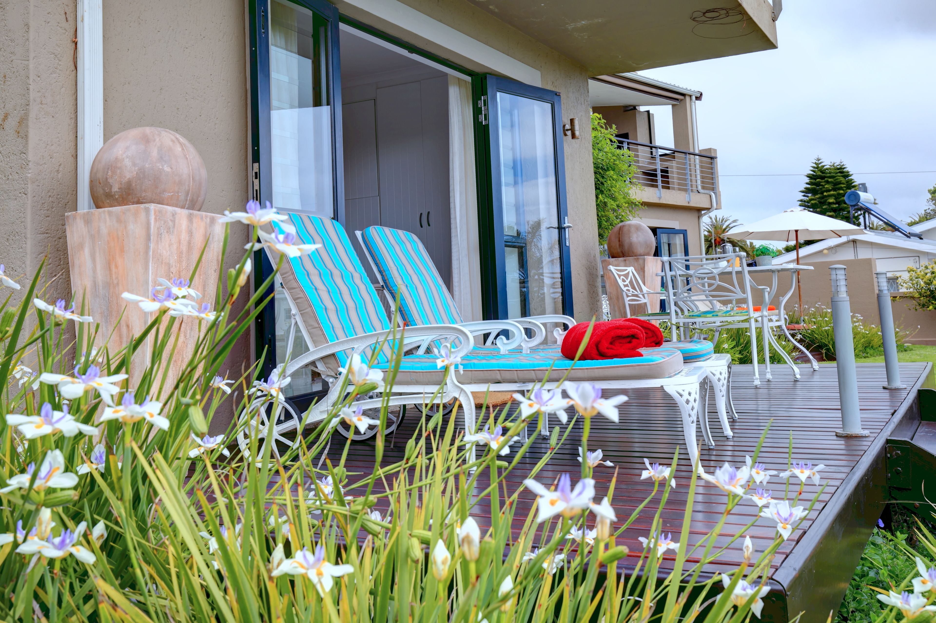 Ein Balkon mit zwei gestreiften Liegestühlen, einem Tisch und einem roten Handtuch.