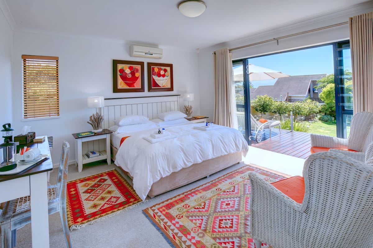 Ein Schlafzimmer mit einem großen Bett, einem Schreibtisch mit Stuhl, einem Balkon mit Korbmöbeln und Kunstwerken an den Wänden.