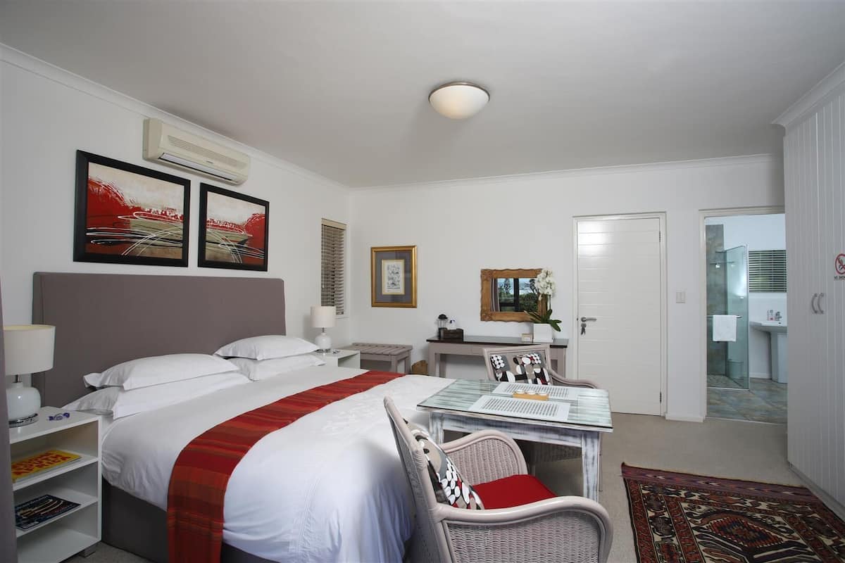 Ein Hotelzimmer mit Bett, Nachttischen, Schreibtisch mit Stuhl, Spiegel und einem durchgehenden Türrahmen einsehbaren Badezimmer.