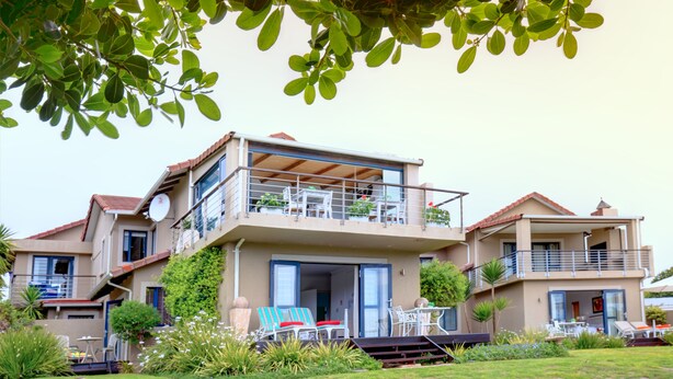 Una casa de dos pisos con balcón, mobiliario exterior y un jardín bien cuidado.