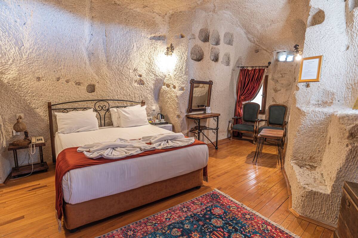 Ein Schlafzimmer mit Stehwand, einem Bett, Holzboden, einem Sessel und einem Schreibtisch mit Spiegel.