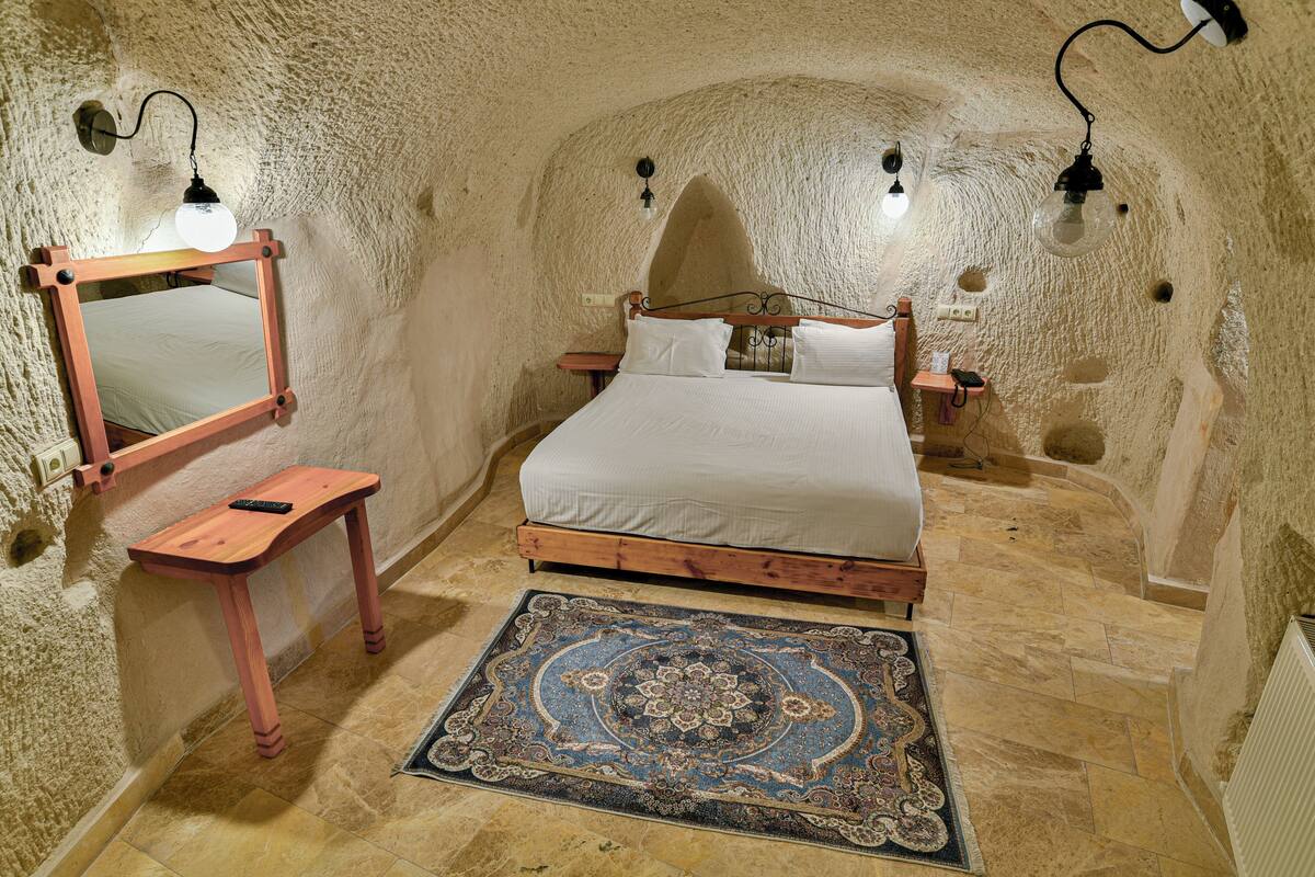 Ein Schlafzimmer mit einem hölzernen Bett, einem kleinen Nachttisch, einem Spiegel und einem gemusterten Teppich.