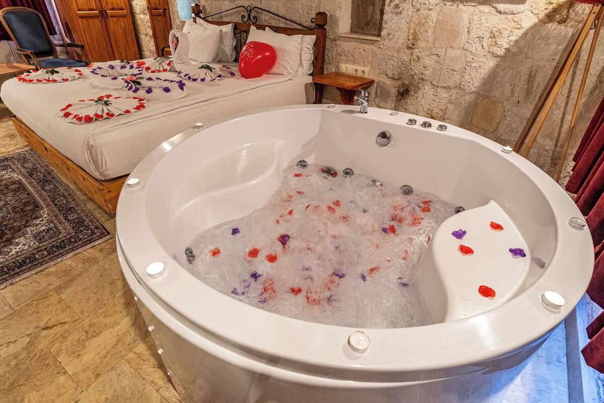 Ein Zimmer mit einer großen Badewanne, gefüllt mit Wasser und Rosenblättern, einem Bett mit einem roten Luftballon und einem hölzernen Kopfteil.