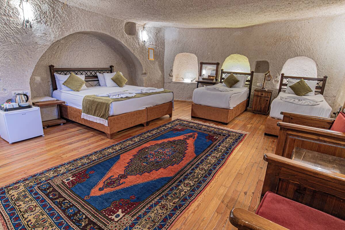 Ein Zimmer mit einem großen Bett, zwei Einzelbetten, Holzmöbeln, einem Teppich und Steinwänden.
