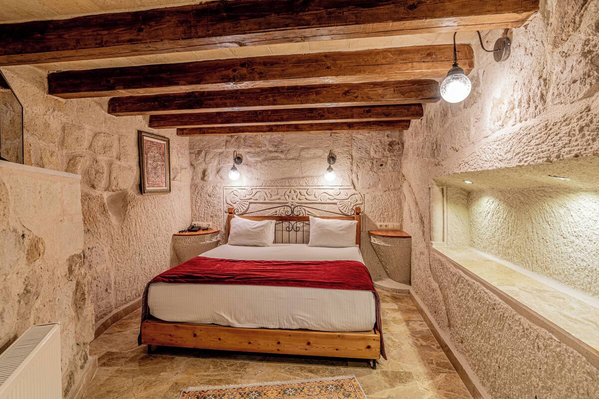 Ein Schlafzimmer mit einem hölzernen Bett, Steinwänden und einer Steinsitzbank.