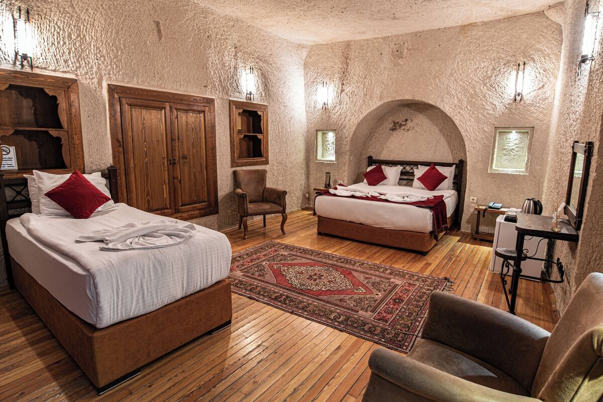 Ein Schlafzimmer mit einem großen Bett, einem kleineren Bett, Holzmöbeln und einer rustikalen Steinwand.