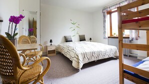 Une chambre avec un lit superposé, un bureau avec des chaises, un miroir et une plante en pot.