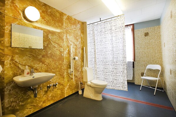 A bathroom with a marble wall, a sink, a toilet, and a shower curtain with text. - Pension Elmehøj (Stege)