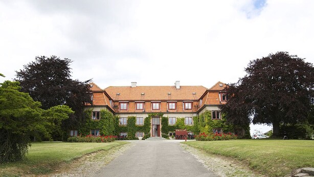 Un grand bâtiment à deux étages, doté d’une façade symétrique, d’une entrée centrale et d’une allée de gravier menant à la façade.