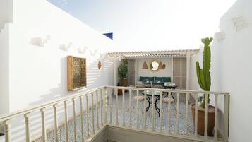 A courtyard with a white wall, a tiled floor, a small table with chairs, and potted plants.