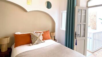 A bedroom with a bed, two nightstands, a wooden headboard, a window with curtains, and a door leading to an outdoor area.