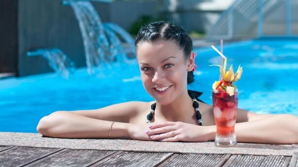 Une personne se détend au bord d’une piscine, un verre à portée de main.