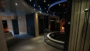 Un espace piscine intérieur moderne, doté d’un jacuzzi circulaire, d’un coin salon et d’un escalier menant à un niveau supérieur.
