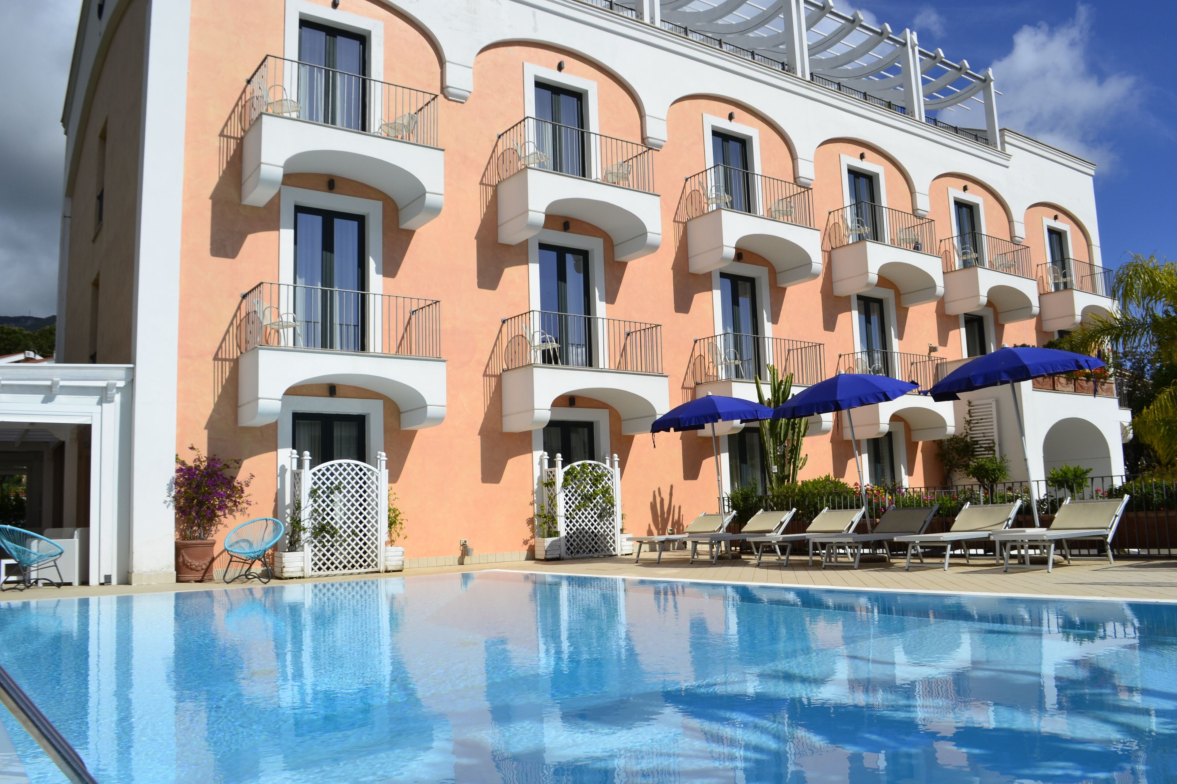 A hotel with a swimming pool, multiple balconies, and lounge chairs.