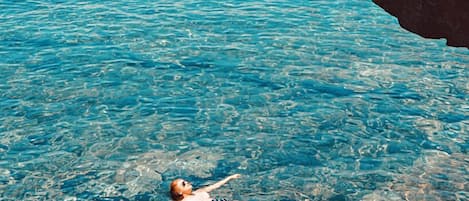 Una persona flota en aguas azules y transparentes cerca de un acantilado rocoso.