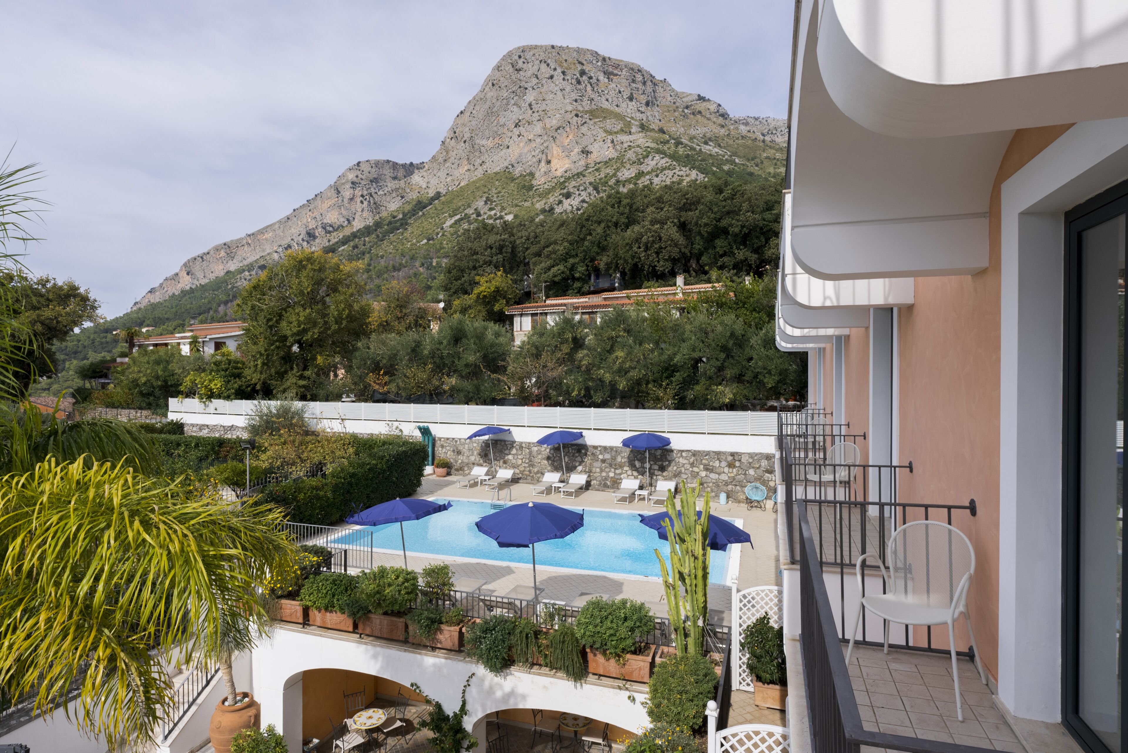 Un espace piscine agrémenté de parasols, une vue sur la montagne et un balcon avec un fauteuil.