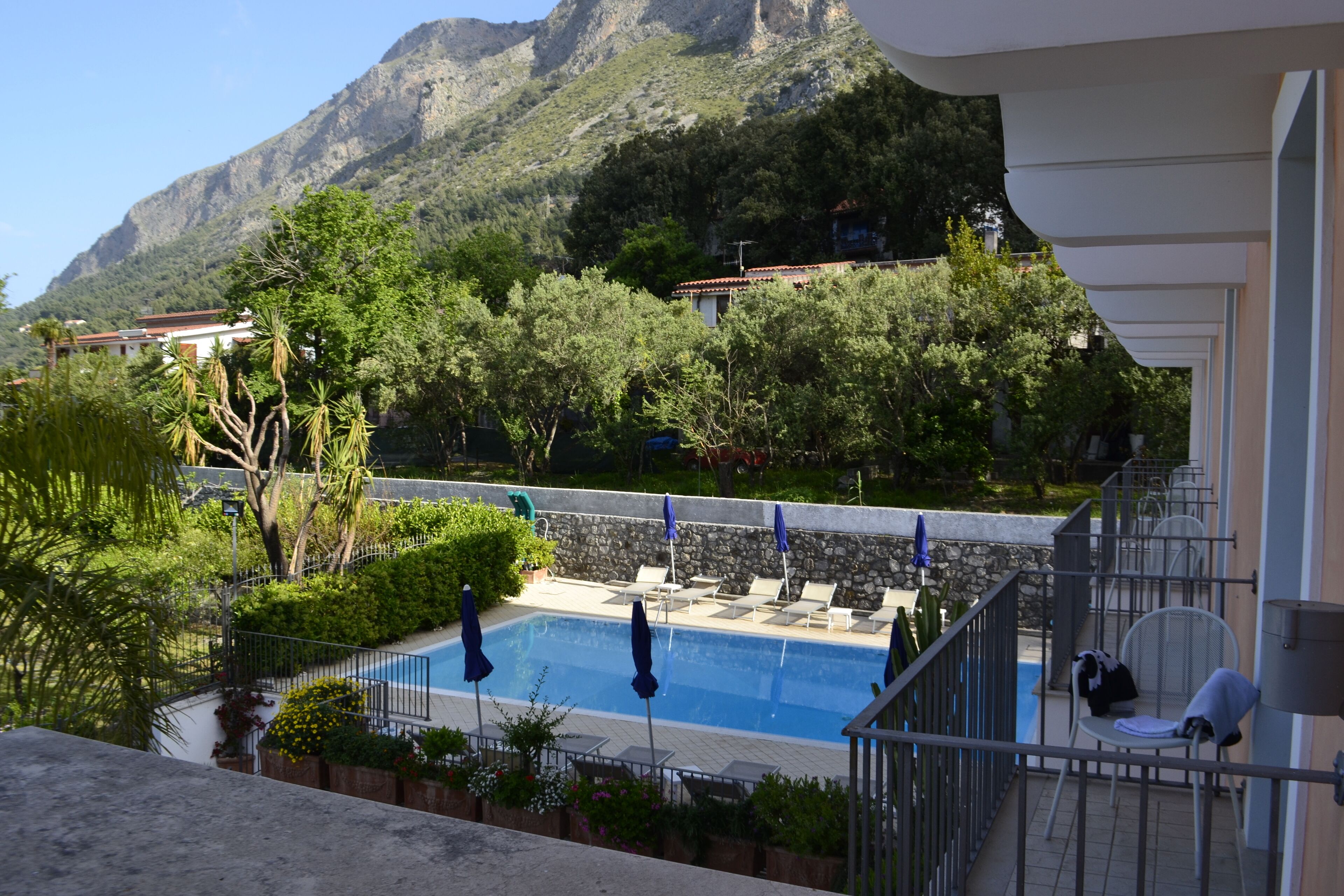 Area piscina con lettini e ombrelloni, circondata da vegetazione e montagne sullo sfondo.
