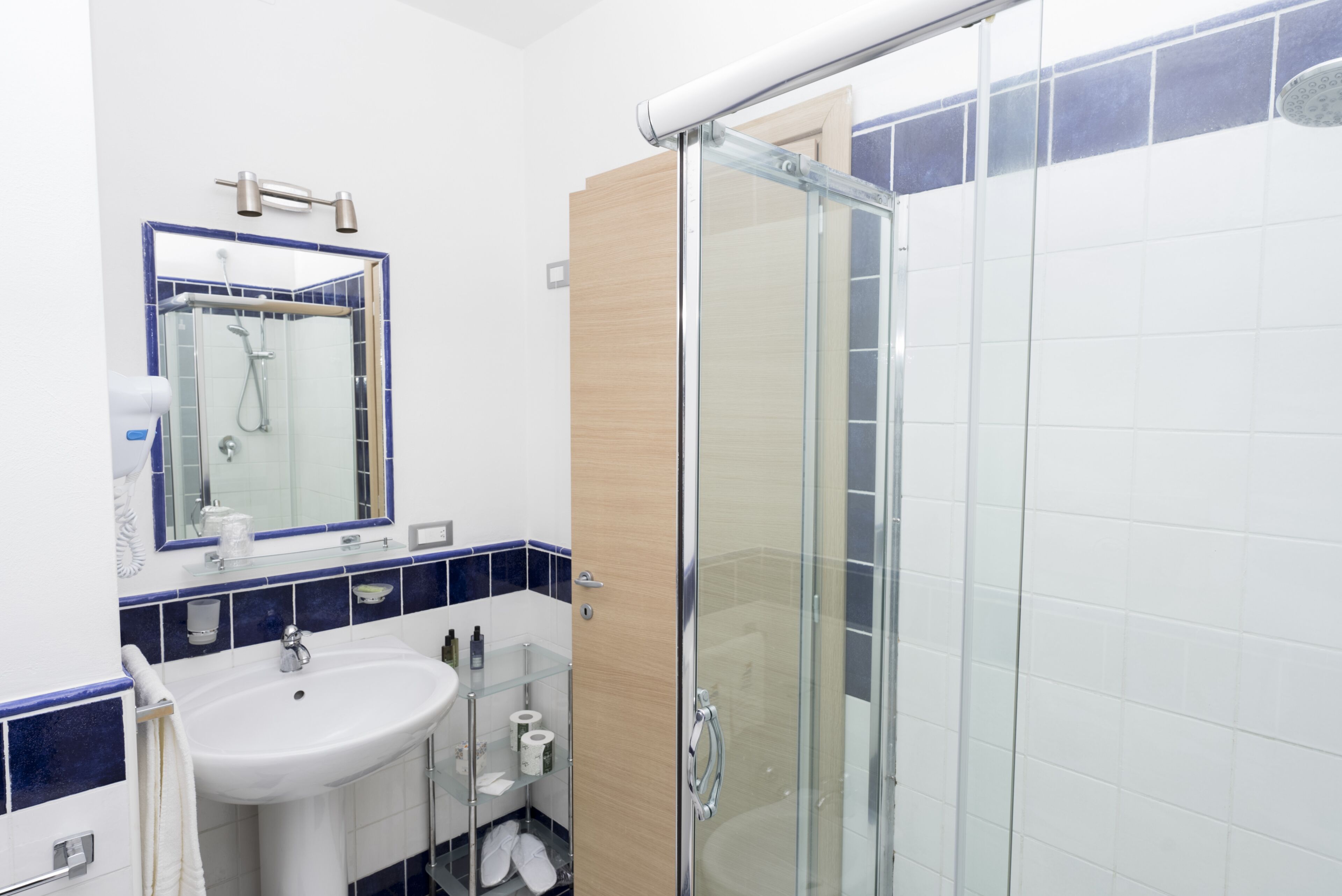 Un baño moderno con ducha de vidrio, lavamanos blanco y espejo con marco azul.