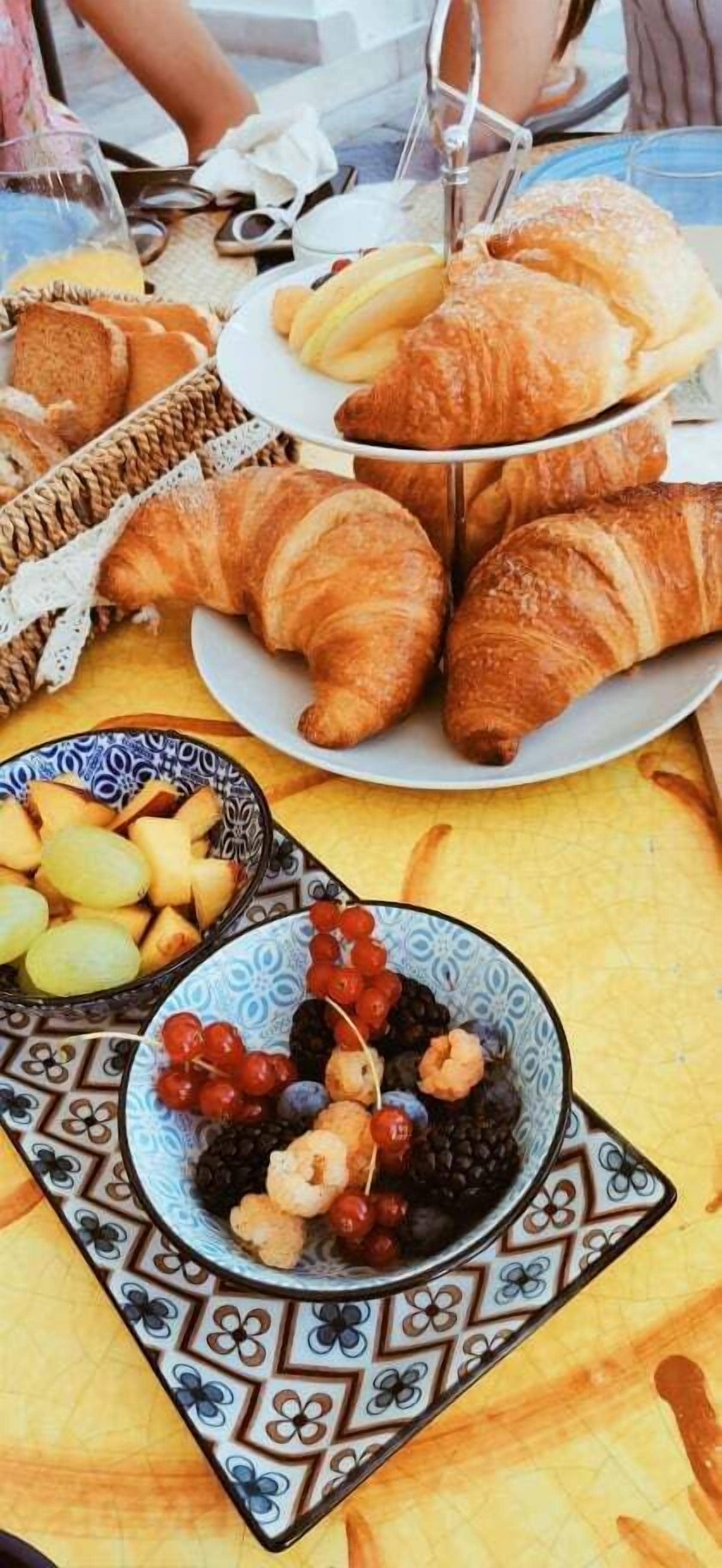 Una mesa con croissants, un bol de fruta y una bandeja de pasteles.