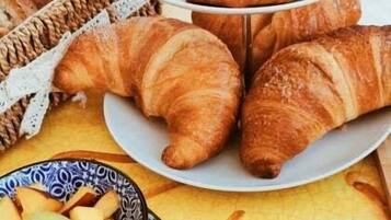Una mesa con croissants, un bol de fruta y una bandeja de pasteles.