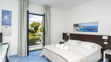 A hotel room with a bed, a desk, a chair, and a balcony with a view of the sea.