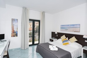 A hotel room with a bed, a desk, a chair, a nightstand, a lamp, and a window with curtains.