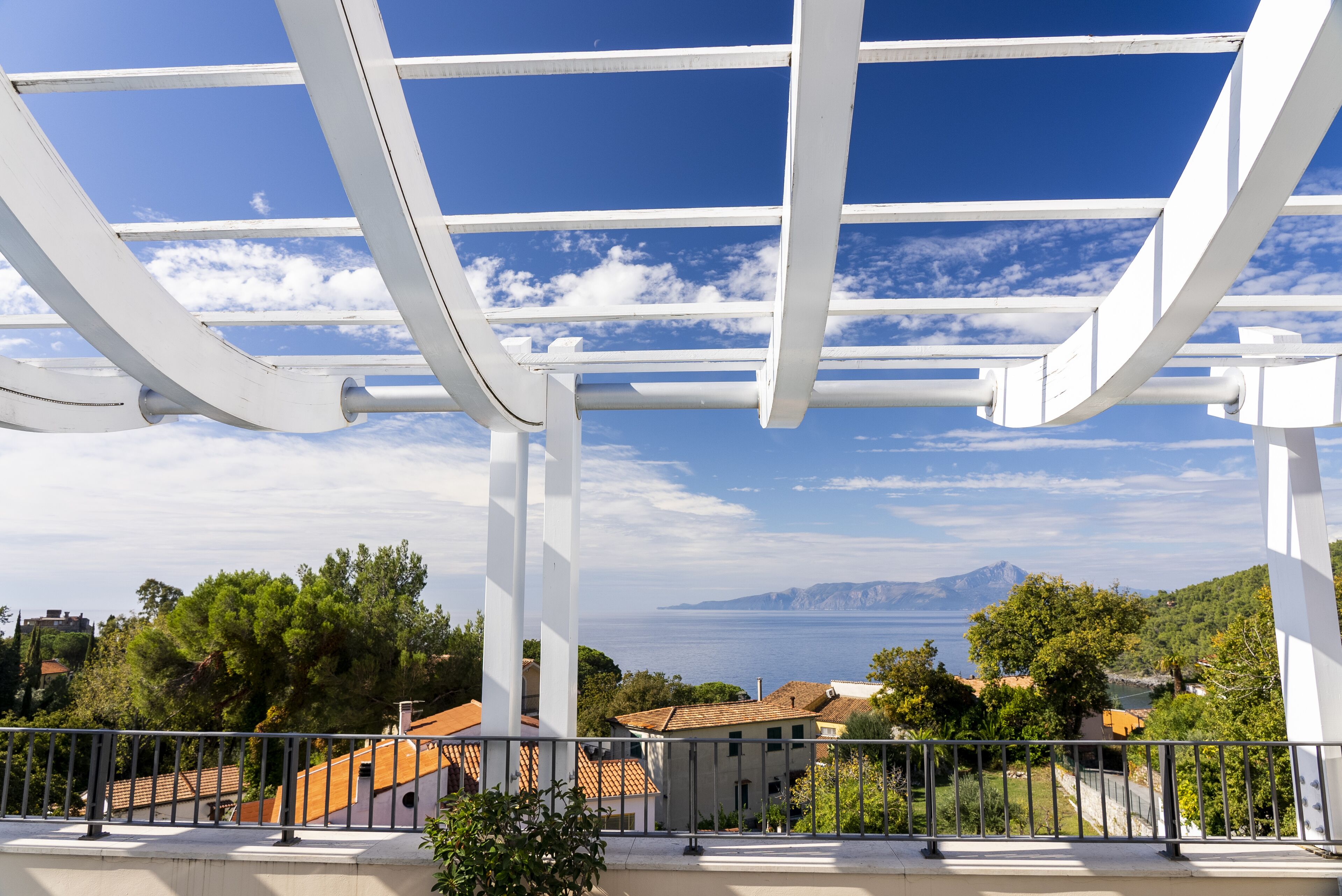 En balkon med gelænder der kigger ud over en kystby med huse og en klar blå himmel.