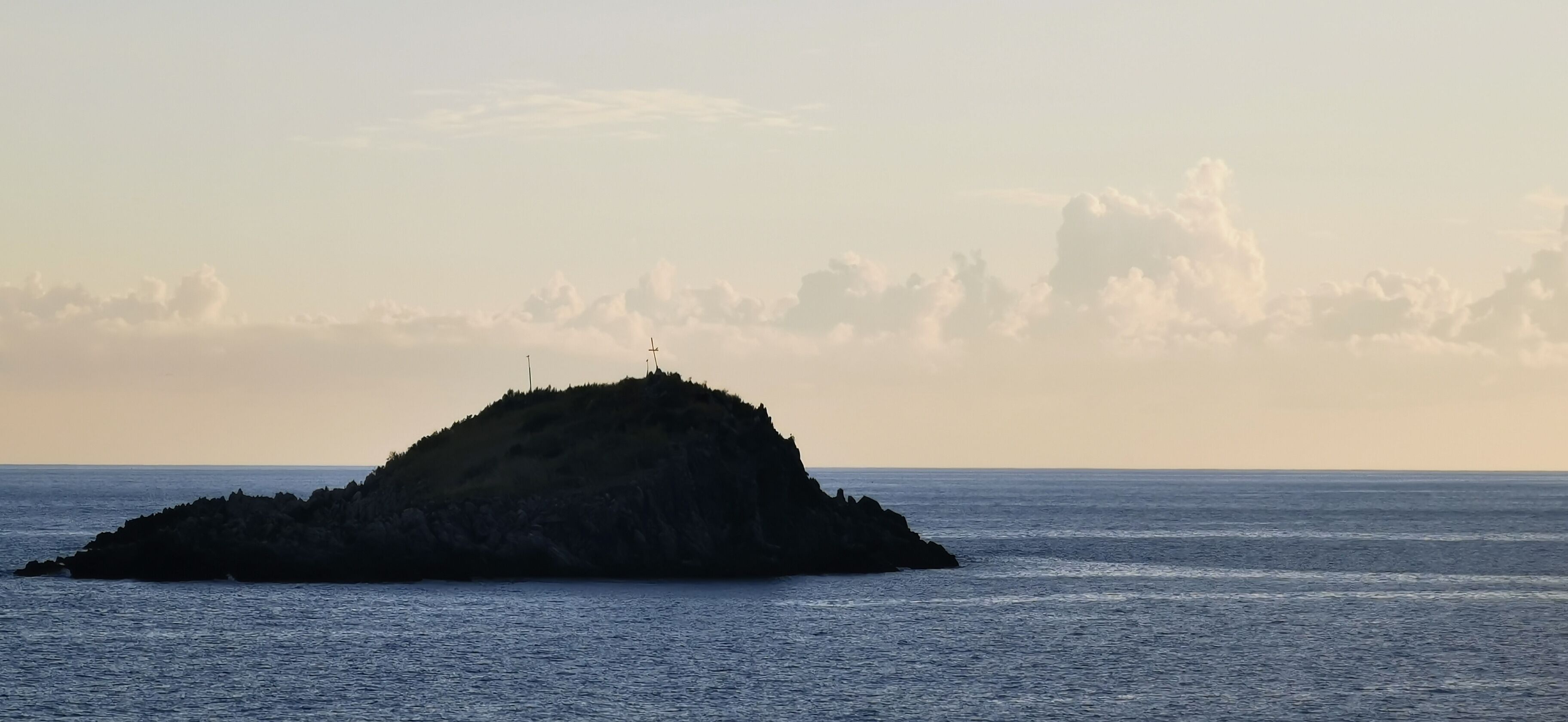 A small island with a cross on top, surrounded by calm sea and a clear sky.