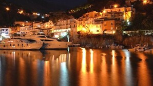 A waterfront marina with yachts docked, surrounded by hillside buildings with warm lighting. - Hotel Murmann (Maratea)