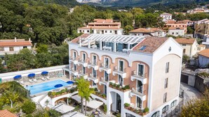 A multi-story hotel with a rooftop pool, outdoor seating, and a view of surrounding mountains. - Hotel Murmann (Maratea)